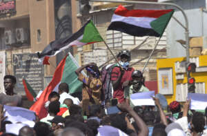 Sudanese demonstrators raise national flags as they take part in a protest in the city of Khartoum Bahri, the northern twin city of the capital, to demand the government's transition to civilian rule, on October 21, 2021. - Supporters of Sudan's transitional government took to the streets of the capital today as rival demonstrators kept up a sit-in demanding a return to military rule. The mainstream faction backs the transition to civilian rule, while supporters of the breakaway faction are demanding the military take over. (Photo by AFP)